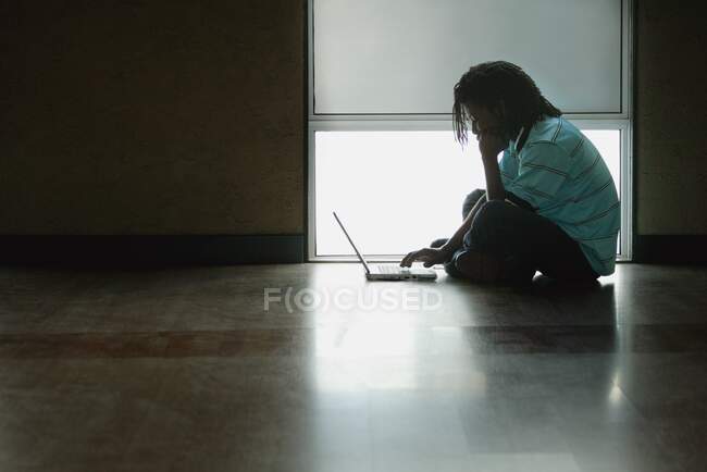 Adolescente sentado en el suelo y trabajando en un ordenador portátil - foto de stock