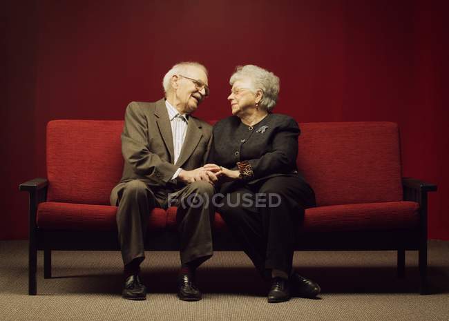 Casal sênior dedicado sentado juntos no sofá vermelho — Fotografia de Stock