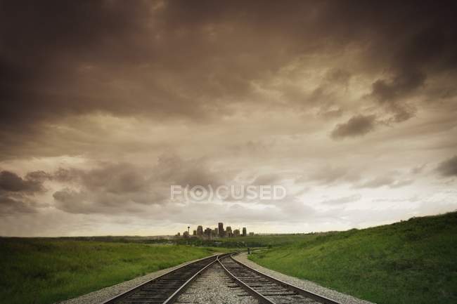 Trilhos ferroviários e cidade distante — Fotografia de Stock