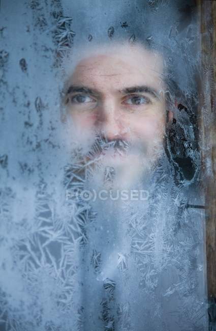 Jeune homme regardant par une fenêtre givrée — Photo de stock