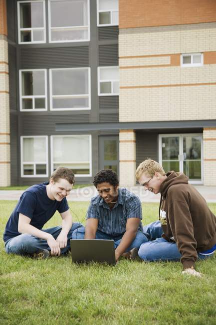Freunde sitzen auf Gras neben dem Gebäude und benutzen einen Laptop — Stockfoto