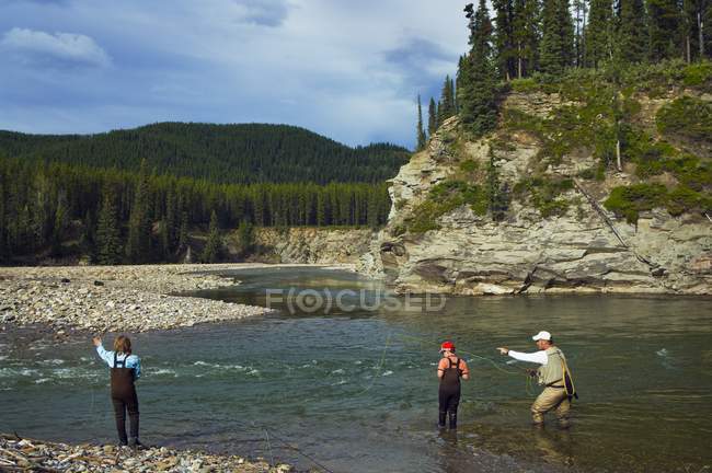 Rear view of father and sons fly fishing in a river — Stock Photo