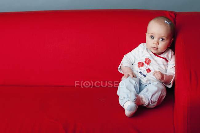 Niña sentada en un sofá rojo - foto de stock
