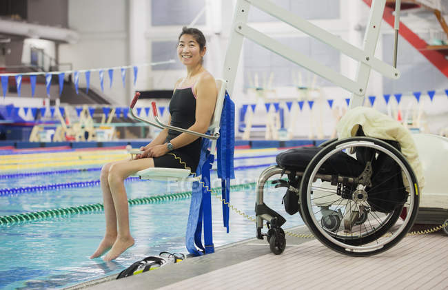 Паралитическая женщина спускается в бассейн на лифте с инвалидной коляской на краю — стоковое фото