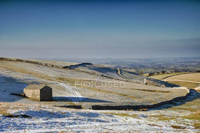 Снежное поле с деревянным сараем — стоковое фото