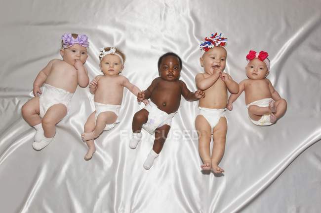 Cinco bebês de fraldas deitados de costas na cama de seda branca — Fotografia de Stock