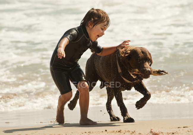 Un garçon court avec un chien sur la plage de Dos Mares devant l'hôtel Dos Mares ; Tarifa, Cadix, Andalousie, Espagne — Photo de stock