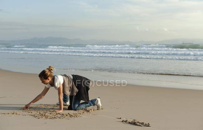 Девушка рисует в песке — стоковое фото