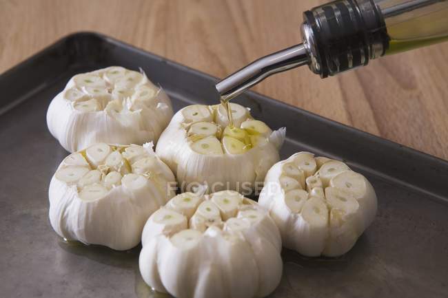 Bulbs of raw garlic on baking sheet with olive oil poured on top — Stock Photo
