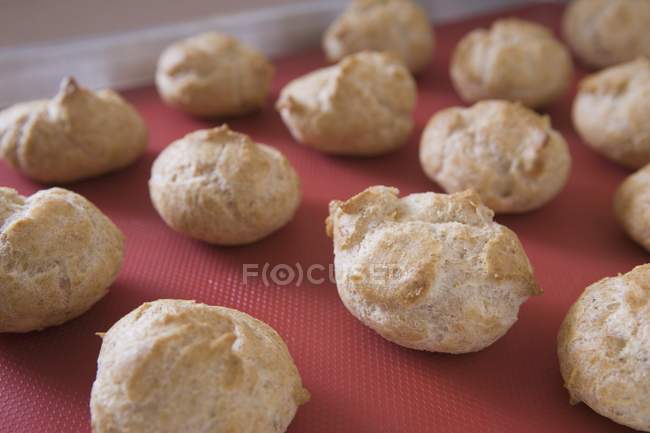 Baked cream puffs on red board — Stock Photo