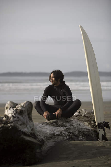 Surfer Sentado en Log On Beach, Cox Bay Cerca de Tofino, British Col. - foto de stock