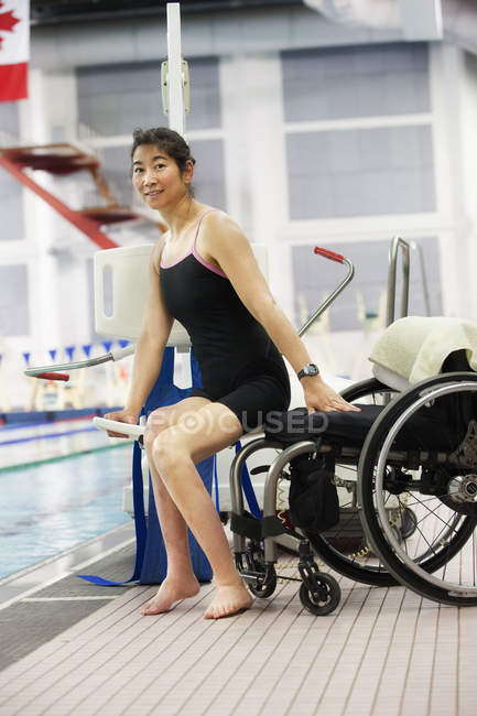 Woman in wheelchair moving onto lift at edge of swimming pool — Stock Photo
