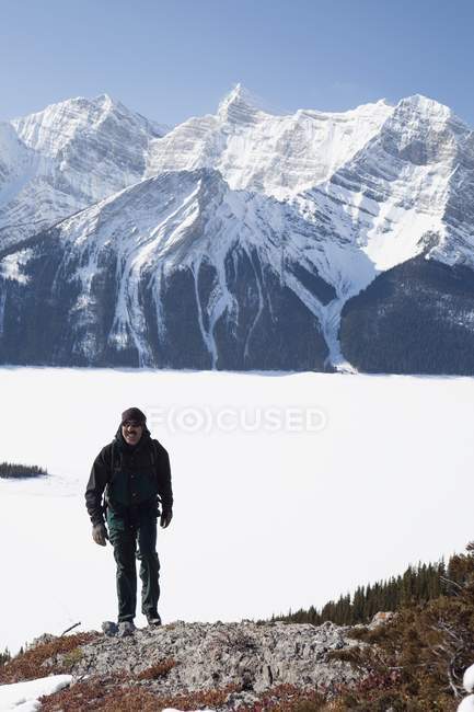 Kananaskis Country, Alberta, Canadá; Un caminante masculino en invierno con montañas cubiertas de nieve y el lago Kananaskis superior - foto de stock