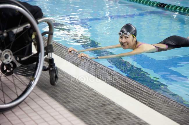 Mulher paraplégica nadando na piscina com cadeira de rodas na borda da água — Fotografia de Stock