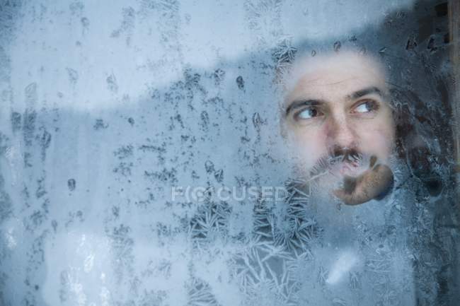 Молодой человек смотрит в замороженное окно — стоковое фото