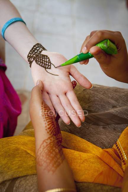 Обрезанный вид индийской женщины, рисующей хну на руке девочки-подростка . — стоковое фото