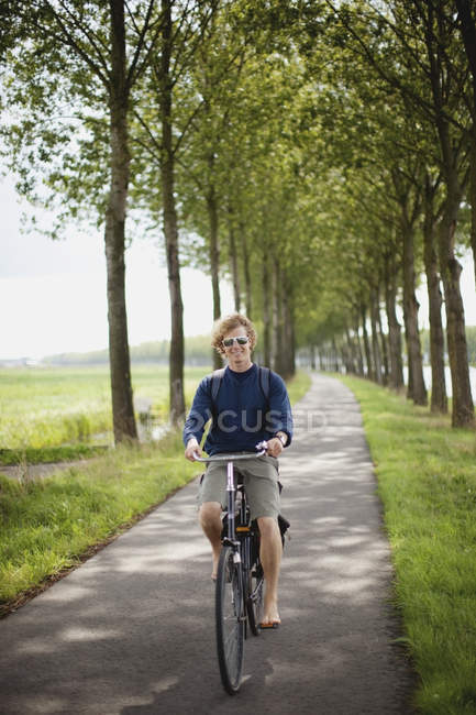 Молодой человек на велосипеде по сельской дороге в Хаутен, Нидерланды — стоковое фото