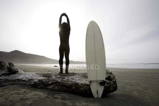 Surfer dehnt sich am Strand in der Nähe von Surfbrett — Stockfoto