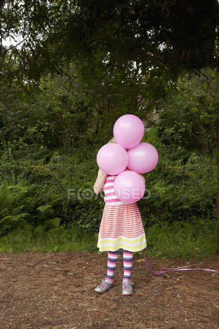 Niña sosteniendo globos rosados en frente de la cara - foto de stock