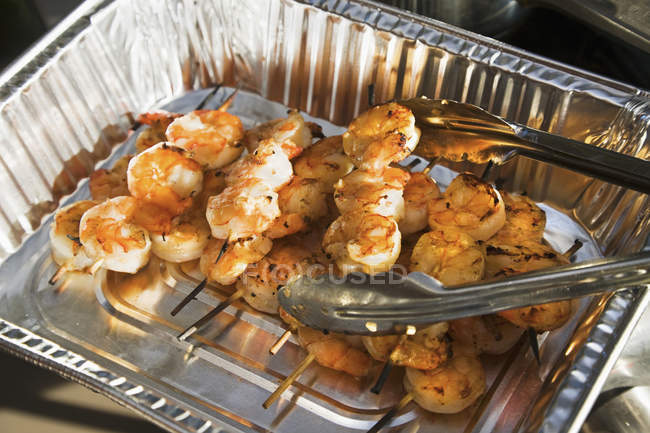 Barbequed shrimp skewers served in foil pan — Stock Photo