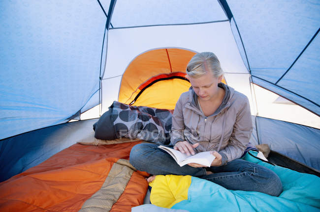 Una giovane donna che legge un libro dentro una tenda; California, Stati Uniti d'America — Foto stock