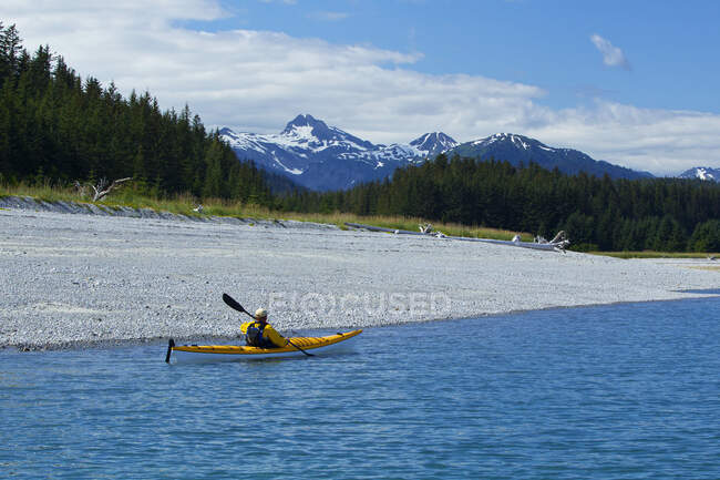 Kayaker de mar remando a lo largo de la costa cerca de Juneau con las montañas de la costa en el fondo, canal de Lynn, sureste de Alaska, verano - foto de stock