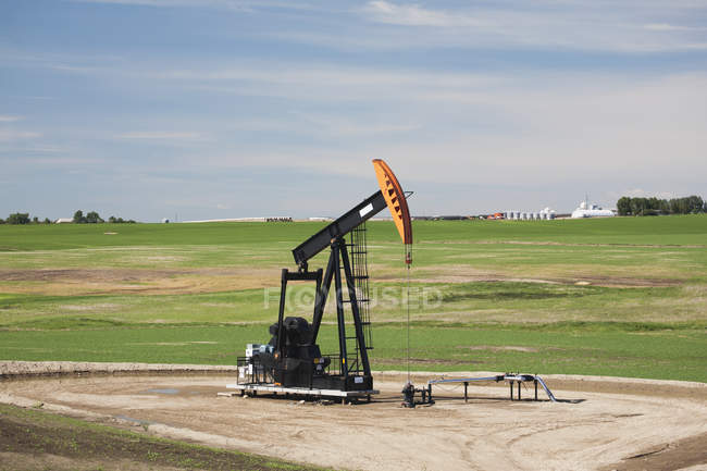 Pumpjack in field with clouds — Stock Photo