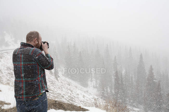 Un hombre toma una foto de un paisaje en la nieve que cae; estados unidos de Colorado de América - foto de stock