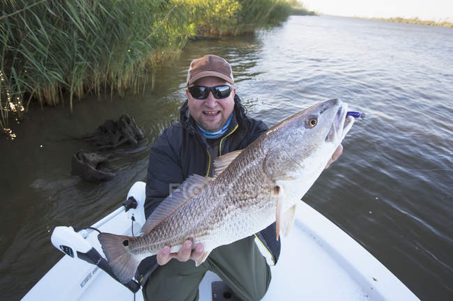 Білий рибалка на човні показує червону рибу на камеру — стокове фото