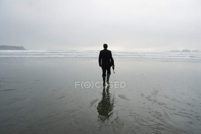 Vista trasera del hombre en la playa húmeda sosteniendo un paraguas - foto de stock