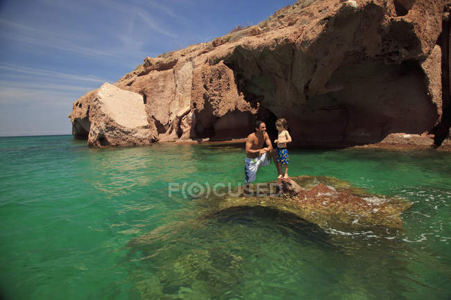 Padre e hijo de pie en la roca en el océano - foto de stock