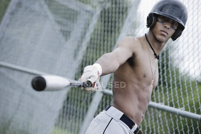 Young adult multiracial man with baseball equipment pointing by bat — Stock Photo
