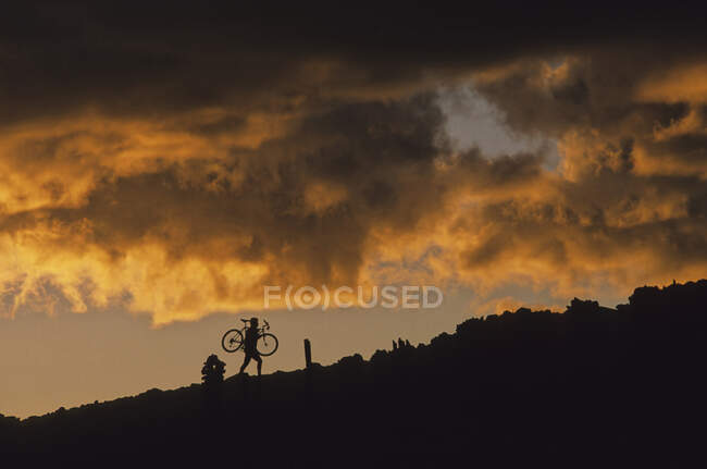 Mountain Biker Carrying Bike Up Rocky Slope, Nuvens de pôr do sol por trás, Whistler, BC Canadá — Fotografia de Stock