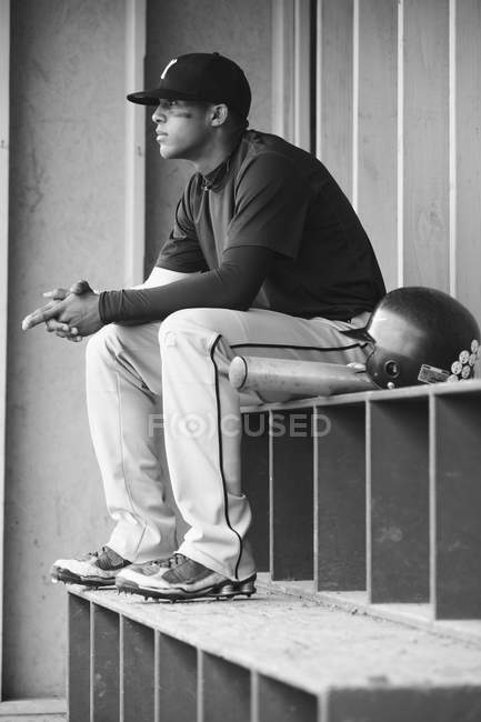 Young multiracial man sitting with baseball equipment, monochrome image — Stock Photo