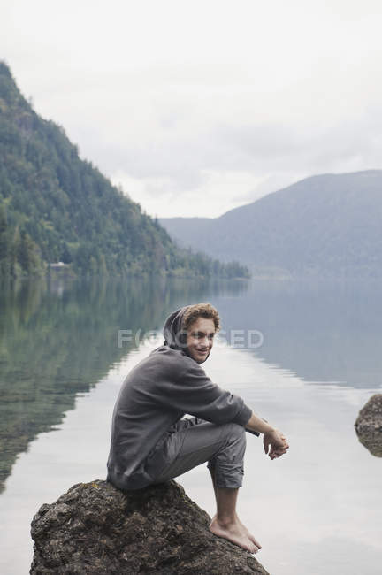 Un joven se sienta en una roca en Cameron Lake; Columbia Británica, Canadá - foto de stock