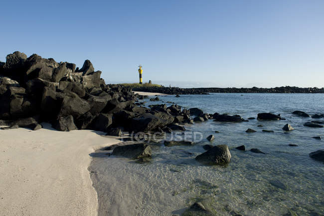 Un faro, rocas y arena blanca - foto de stock