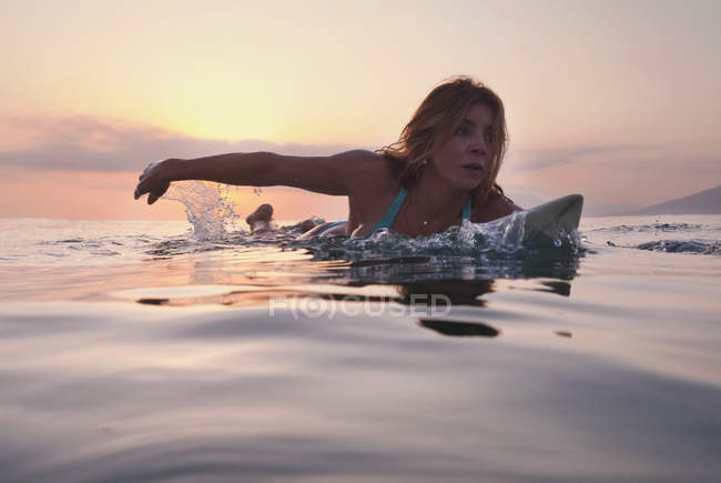 Mujer acostada en la tabla de surf y viendo la puesta de sol - foto de stock