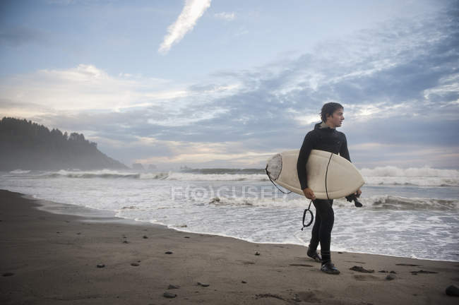 Молодий чоловік з дошкою для серфінгу, що йде вздовж пляжу — стокове фото