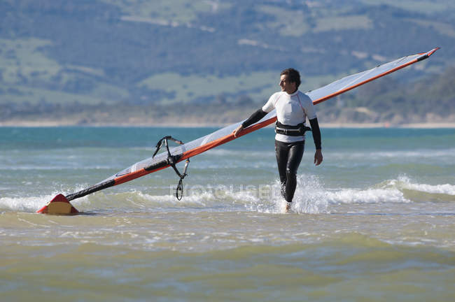 Lateinamerikanischer Windsurfer trägt Surfbrett am Strand — Stockfoto