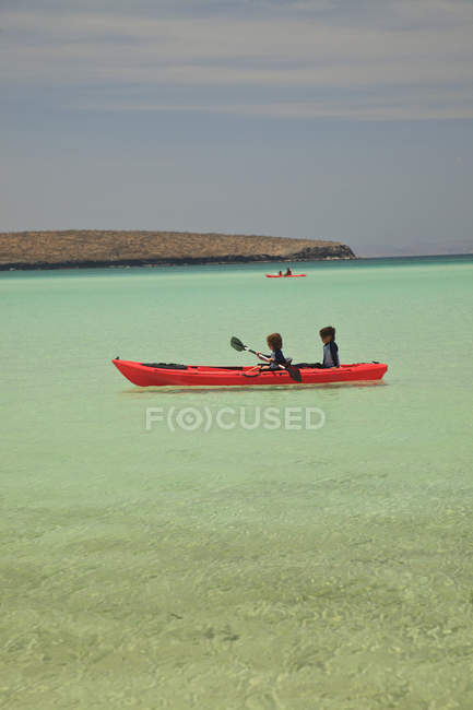 Due giovani ragazzi che remano in una barca rossa al Parco Nazionale Marino Los Islotes Espiritu Santo Island; La Paz, Baja, California, Messico — Foto stock