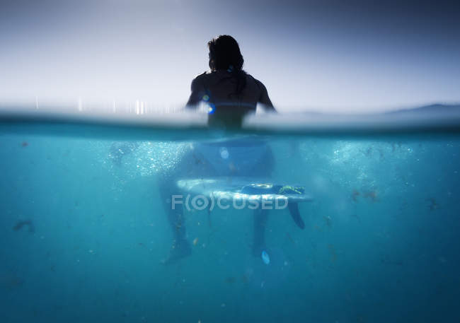 Вид сзади женщины, сидящей на доске для серфинга в воде — стоковое фото