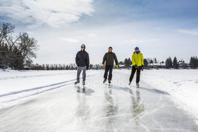 Двоє чоловіків і одна жінка катаються на свіжому доглянутому льоду на ставку — стокове фото