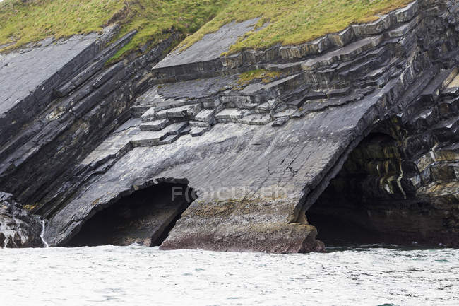 Large rock cave at water edge in cliff side — Stock Photo
