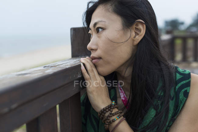 Молода жінка сидить на дерев'яних перилах і дивиться на океан — стокове фото