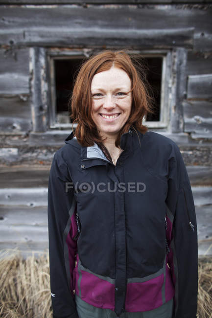Retrato de una mujer con el pelo rojo de pie y un edificio de madera en el fondo - foto de stock