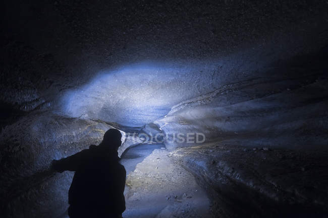 Un hombre usa su faro para iluminar el interior de un largo túnel dentro del glaciar Castner en la cordillera de Alaska; Alaska, Estados Unidos de América - foto de stock