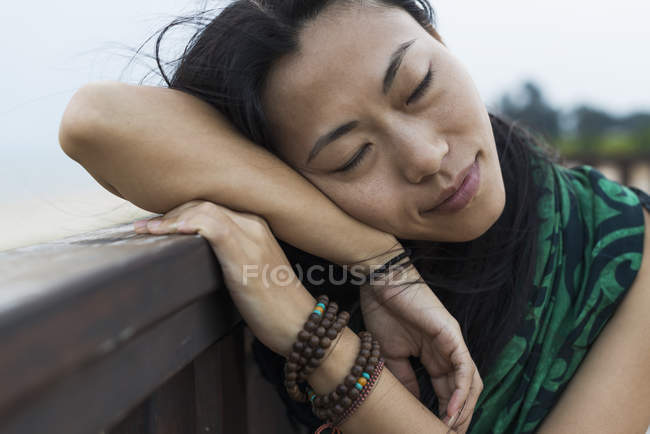 Молодая женщина прислонилась головой к деревянным перилам на пляже — стоковое фото