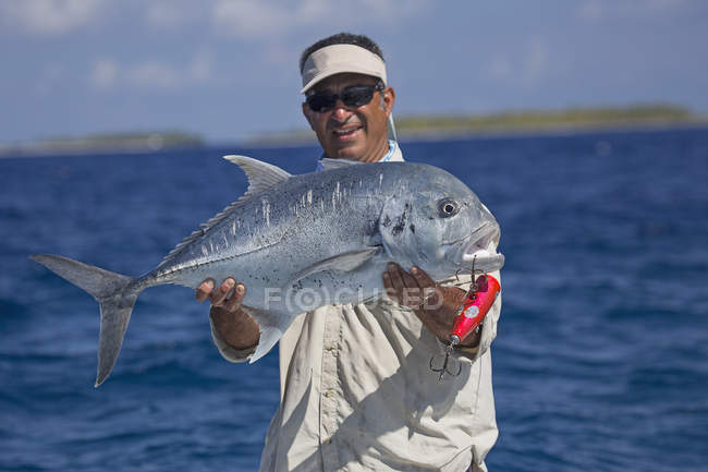 Fisherman on boat holding fresh caught giant trevally fish — Stock Photo