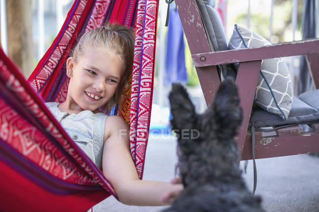 Дівчина розслабляється в гамаку і пестить собаку — стокове фото