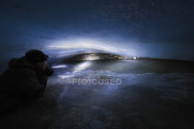 Um homem em uma caverna apertada dentro da geleira de Fels (comumente erroneamente grafada como geleira de enguia) brilha uma luz em uma corrente que flui sob a geleira no inverno; Alaska, Estados Unidos da América — Fotografia de Stock